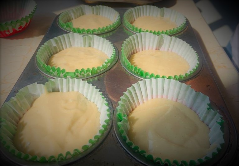 Se observan seis cápsulas de papel en un molde para cup cake, con mezcla de batido con harinas alternativas.