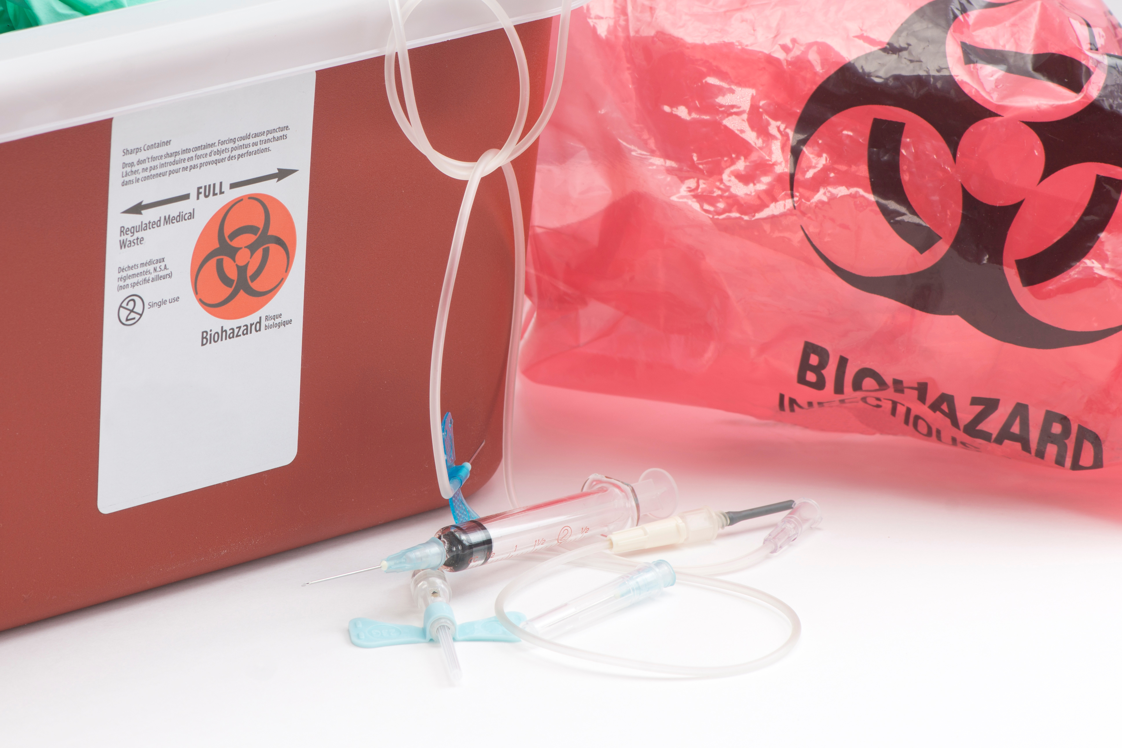 Fotografía de jeringas, y un recipiente de desechos biopeligrosos rojo
