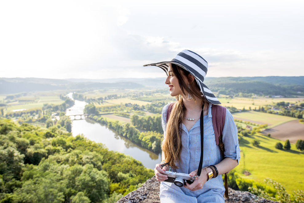 Joven turista disfrufando el paisaje de un río para fotografiarlo