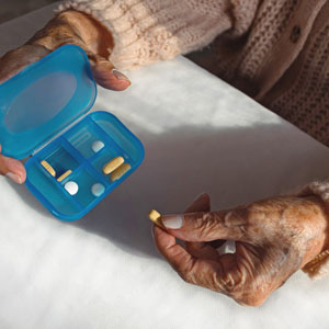 manos de una persona adulta mayor sacando un medicamento de su pastillero.